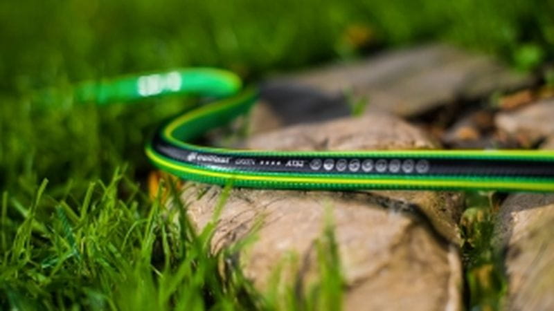 Zielony wąż ogrodowy na trawie i kamieniu